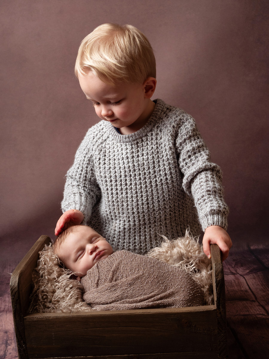 Big brother looking down at his newborn sibling during a photoshoot in Durham