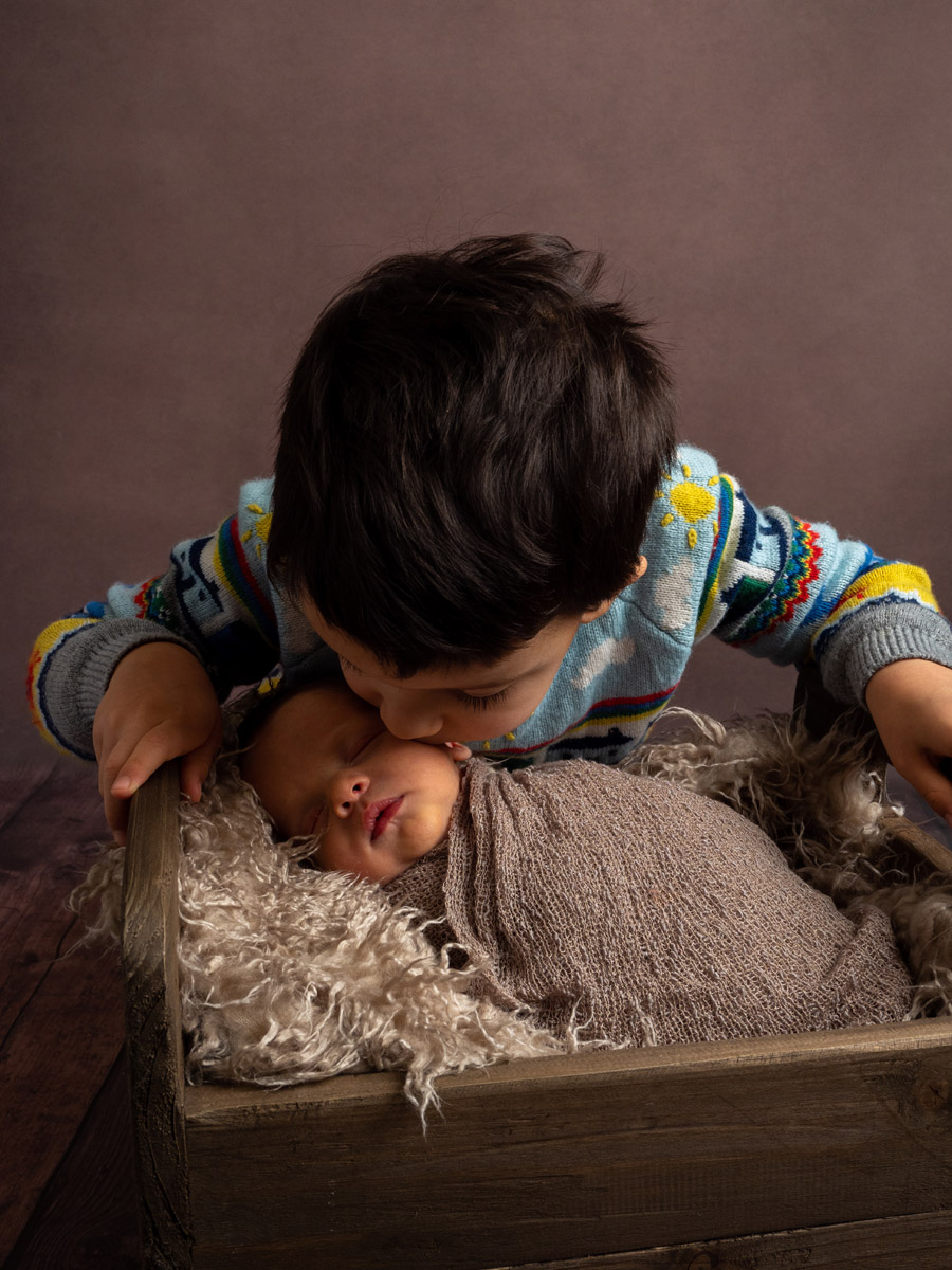 Boy kissing his baby brother during a baby photoshoot
