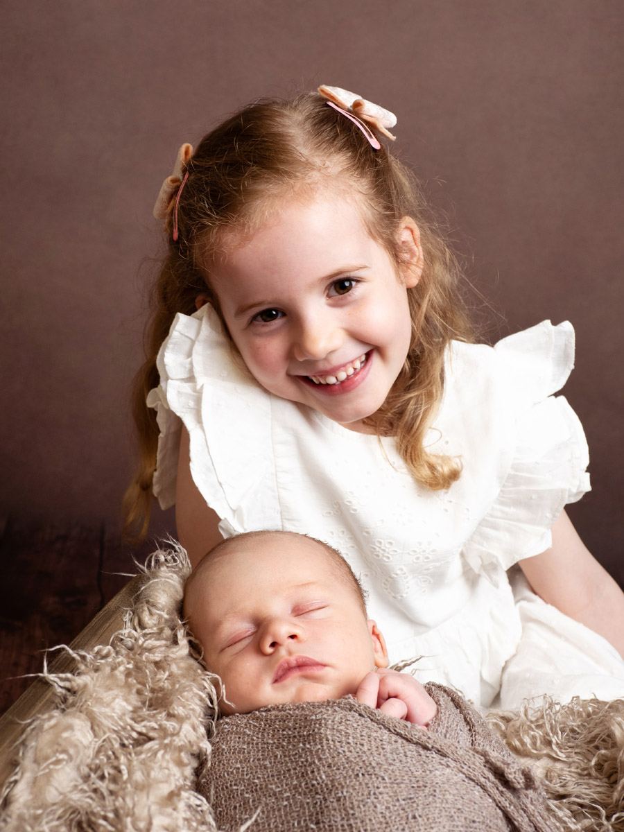 Big smile on a little girl having her photograph taken with her new baby brother