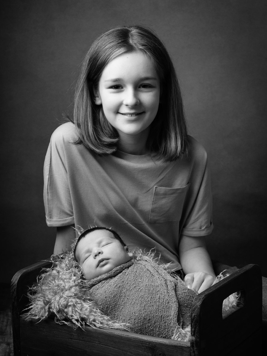 Black and white photo of a sister sitting with her new baby brother