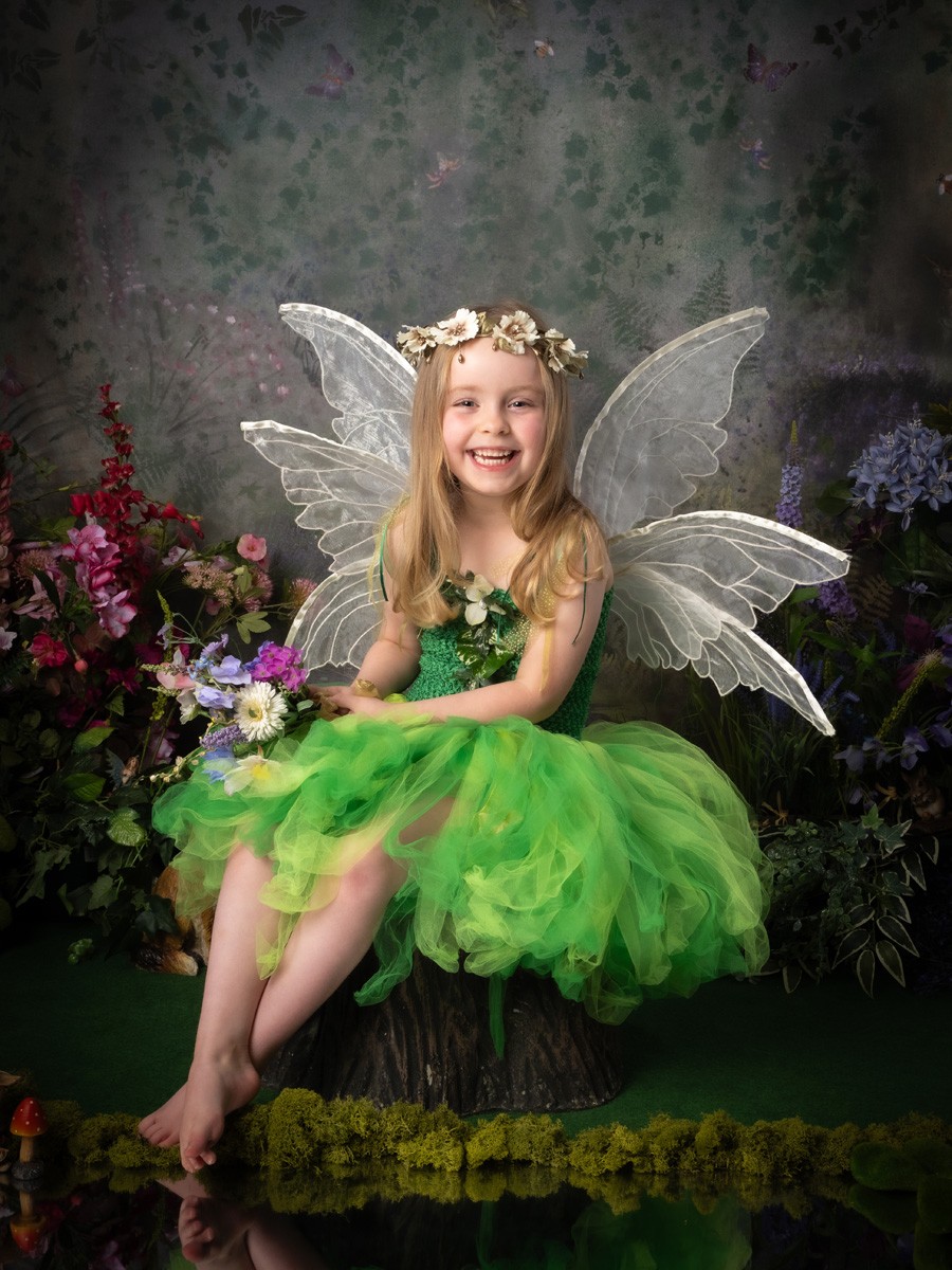 Laughing fairy in a green tutu sitting on a tree stump