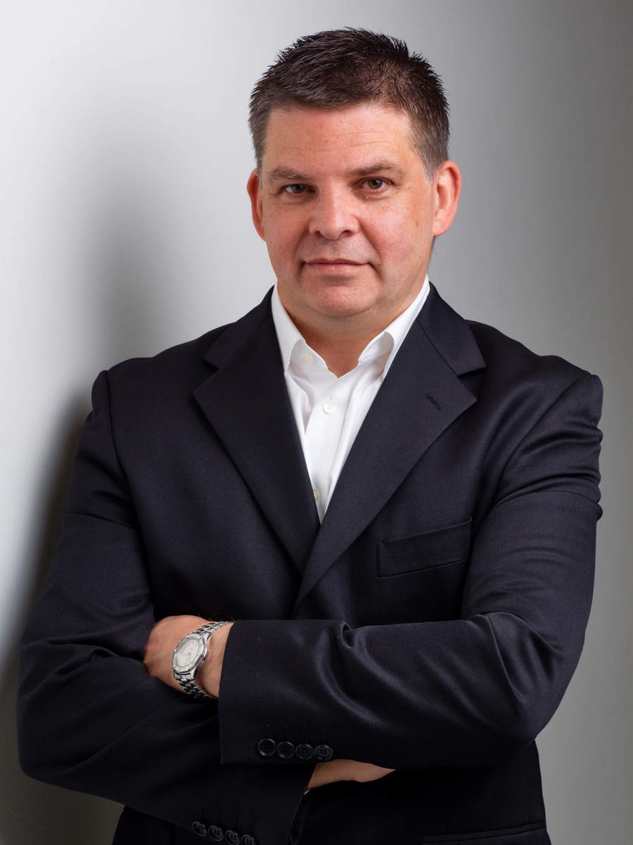 Business portrait of a man in a dark suit with his arms folded on grey