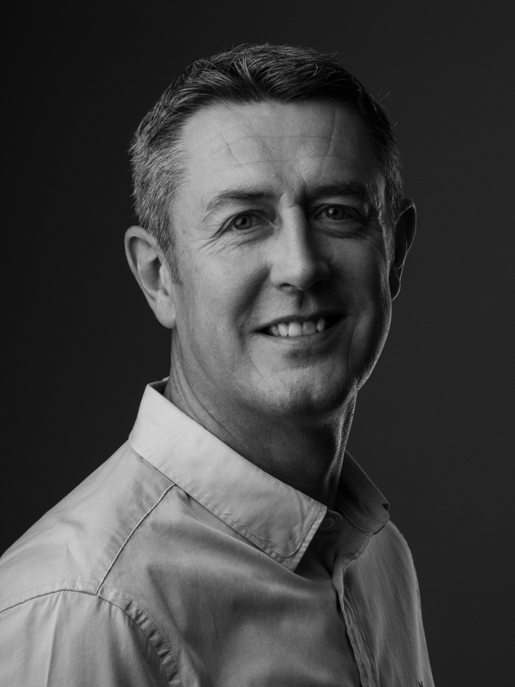 Low key business headshot of a smiling man in a white shirt, black and white
