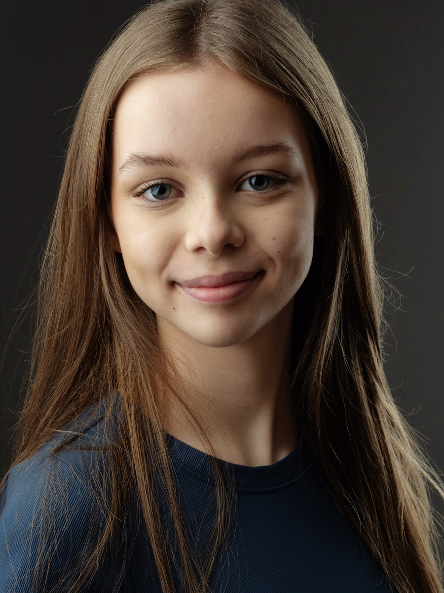 Colour headshot of a smiling teenage girl with long hair on grey