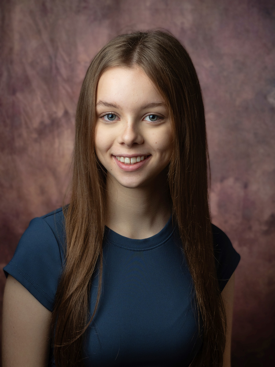 Smiling teenage girl in a navy top against a painted backdrop