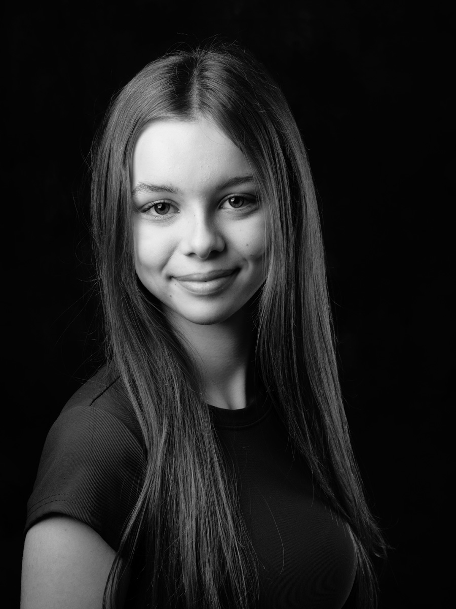 Smiling teenage girl with long hair on a black background, black and white