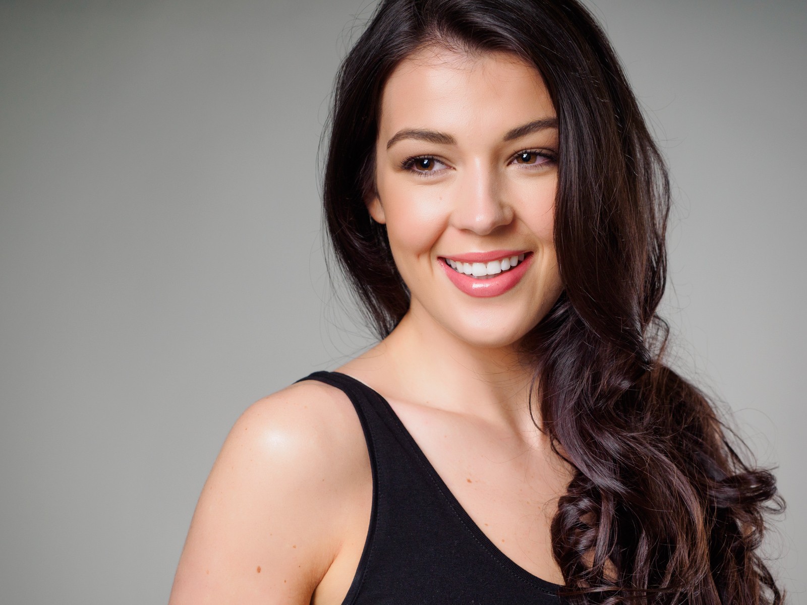 Smiling woman with long dark hair in a black top on grey