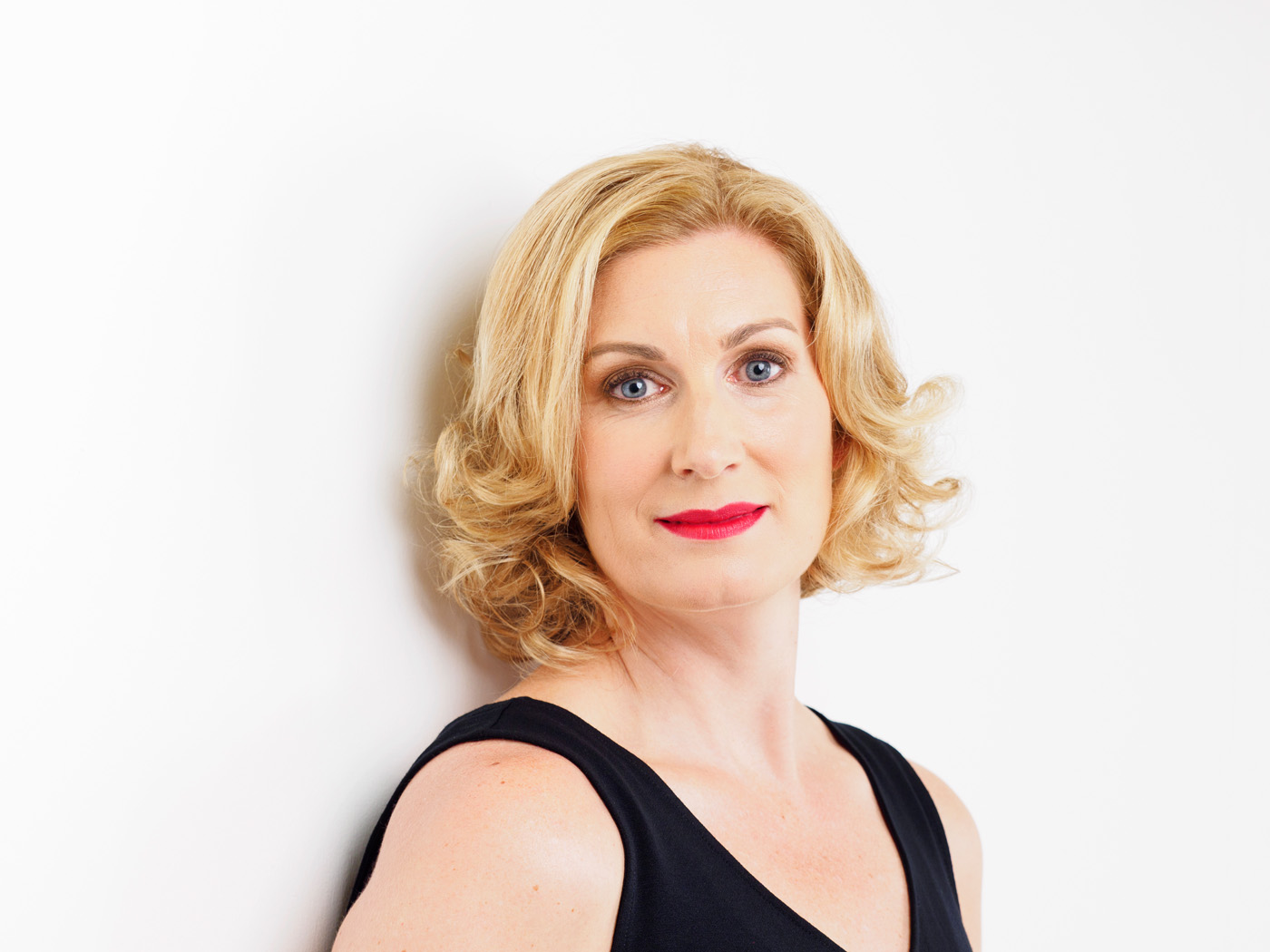 Headshot of a woman with curled blonde hair and red lipstick on white