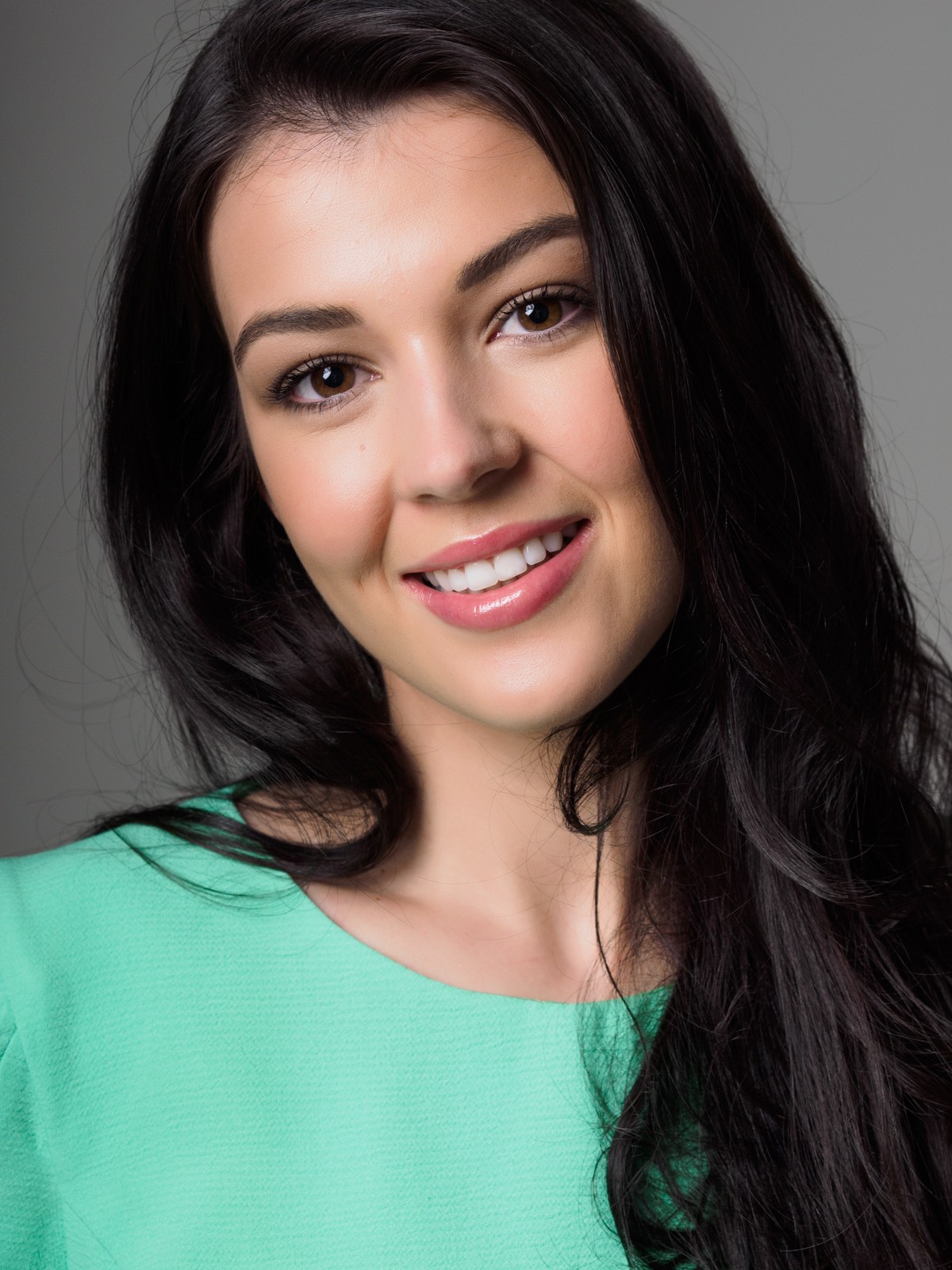 Smiling woman with long dark hair in a green top on grey