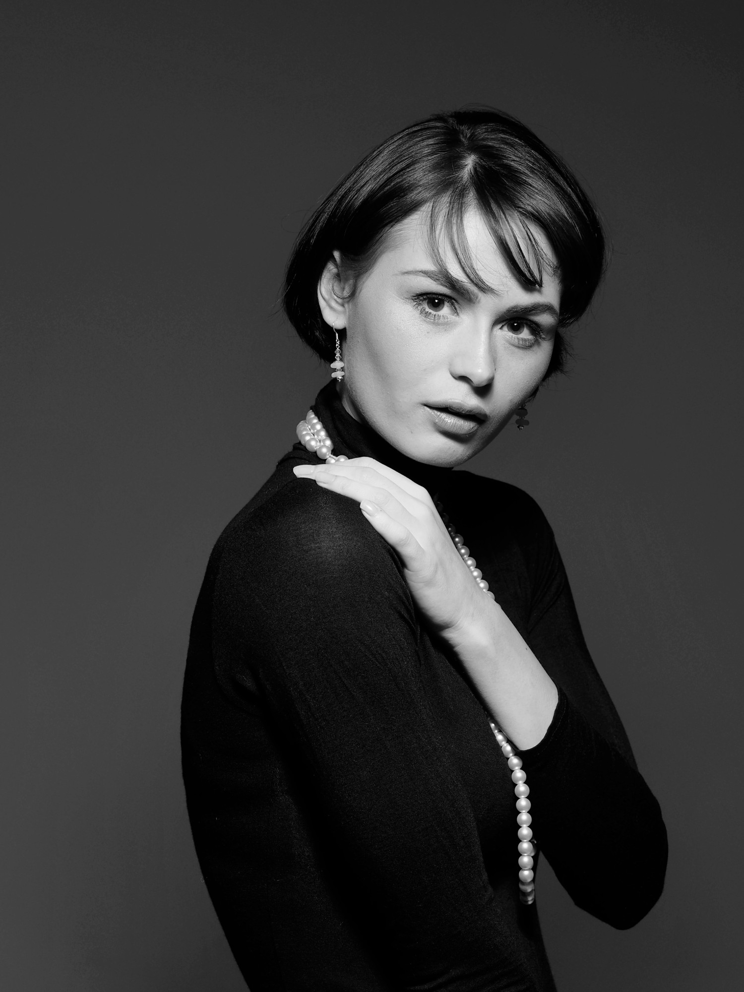 Woman with a short bob and pearls in a black polo neck, black and white