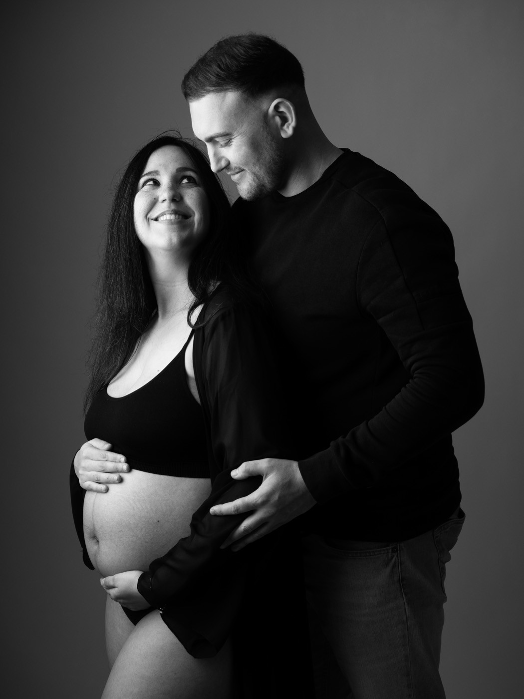 Smiling couple, his hands on her bump, black and white