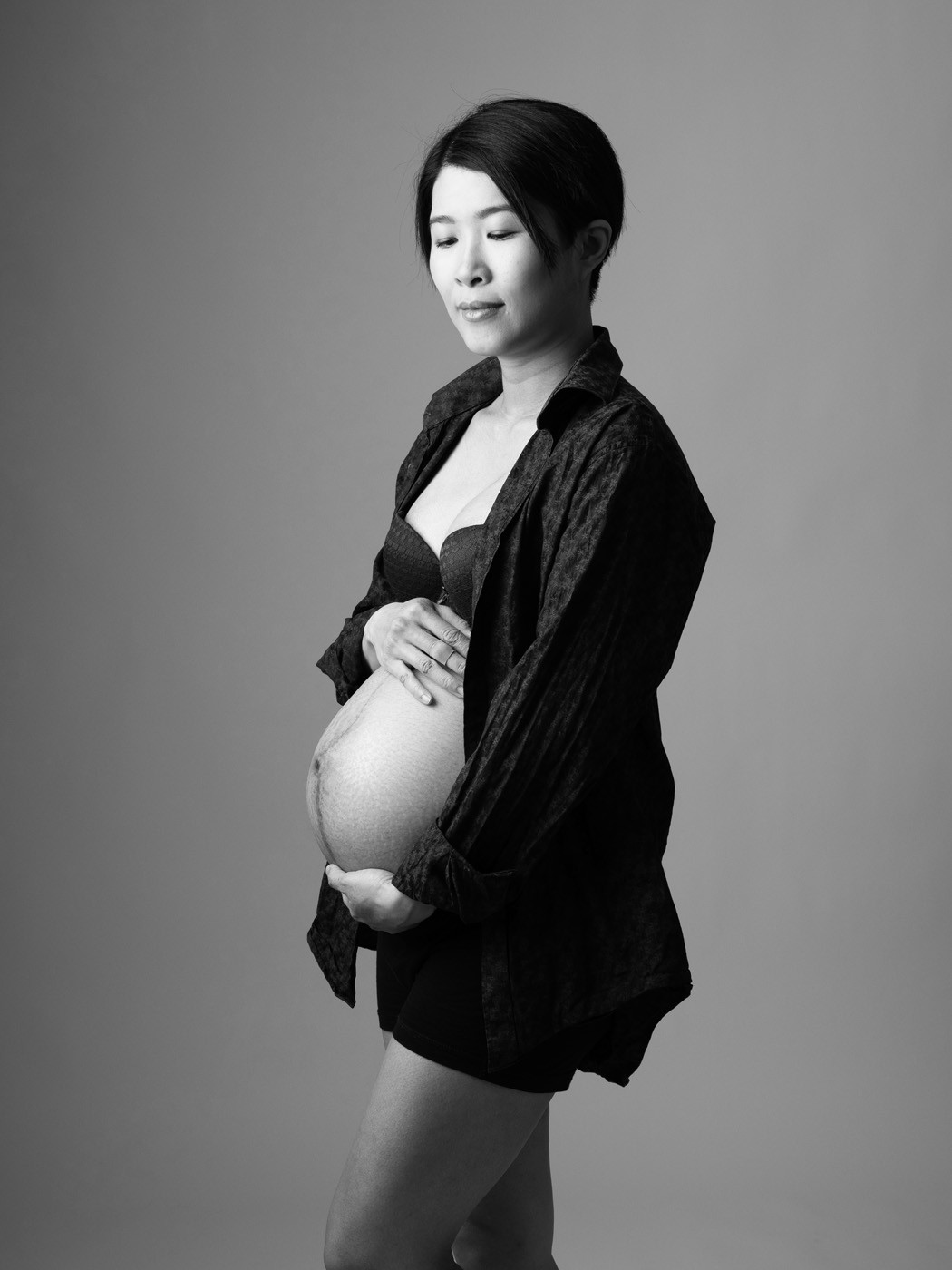 Mum-to-be in an open shirt cradling her bump, black and white