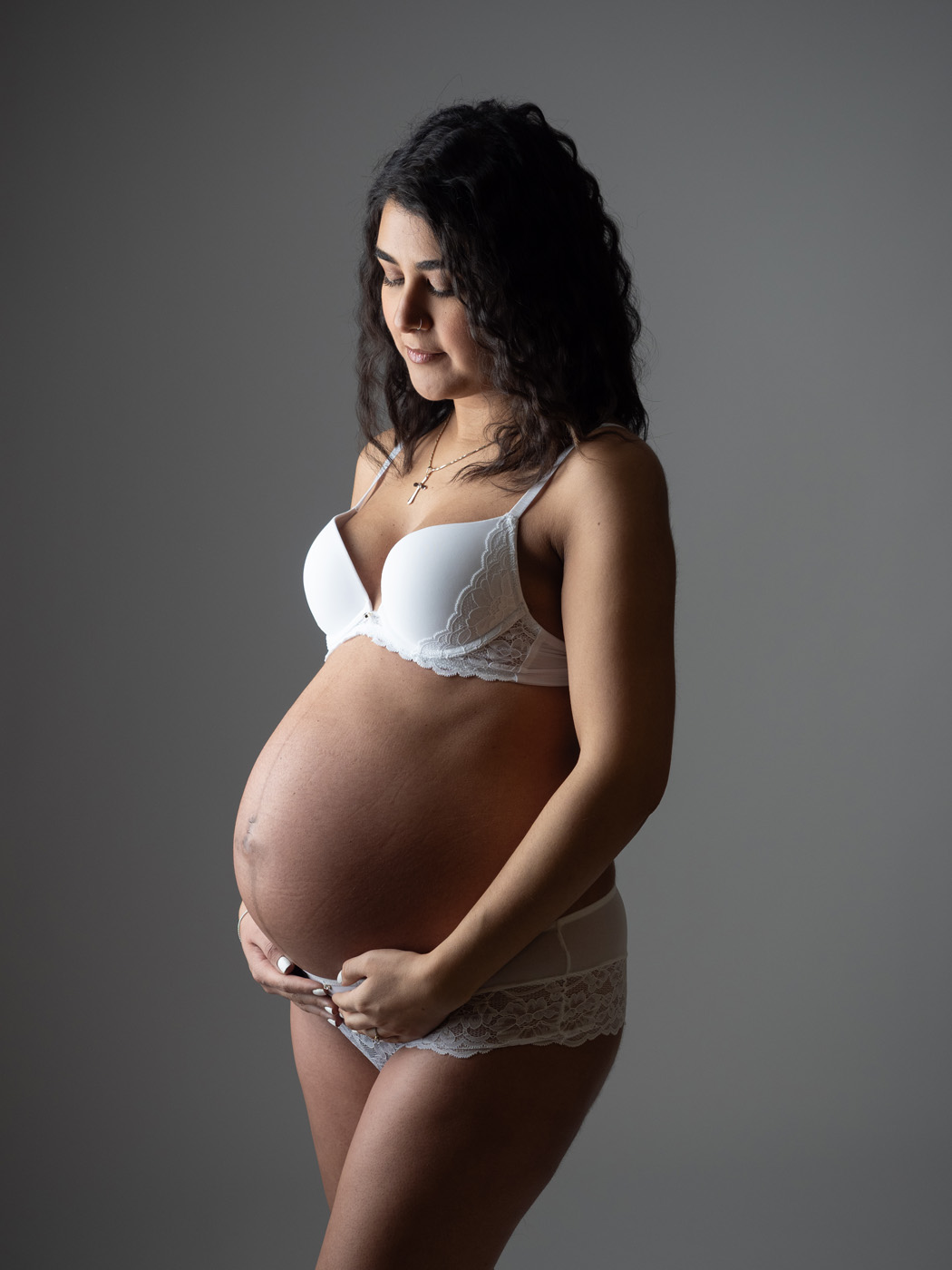 Mum-to-be in white lace looking down at her bump