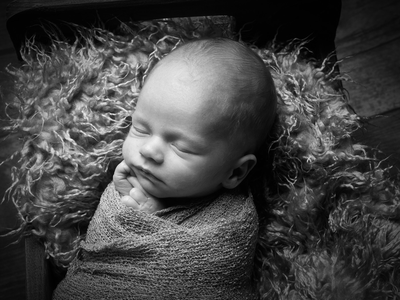 Sleeping newborn wrapped on a sheepskin, black and white