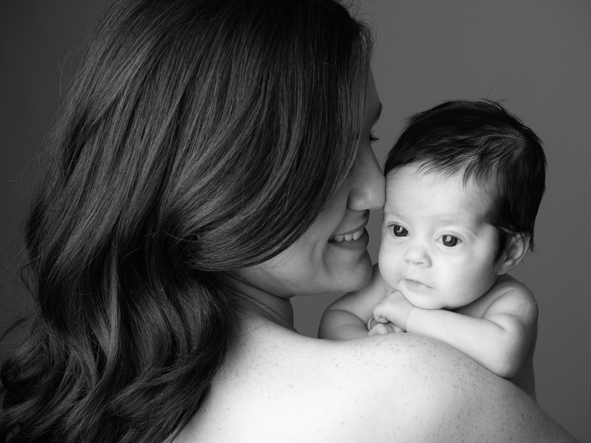 Smiling mum with her newborn peeping over her shoulder, black and white