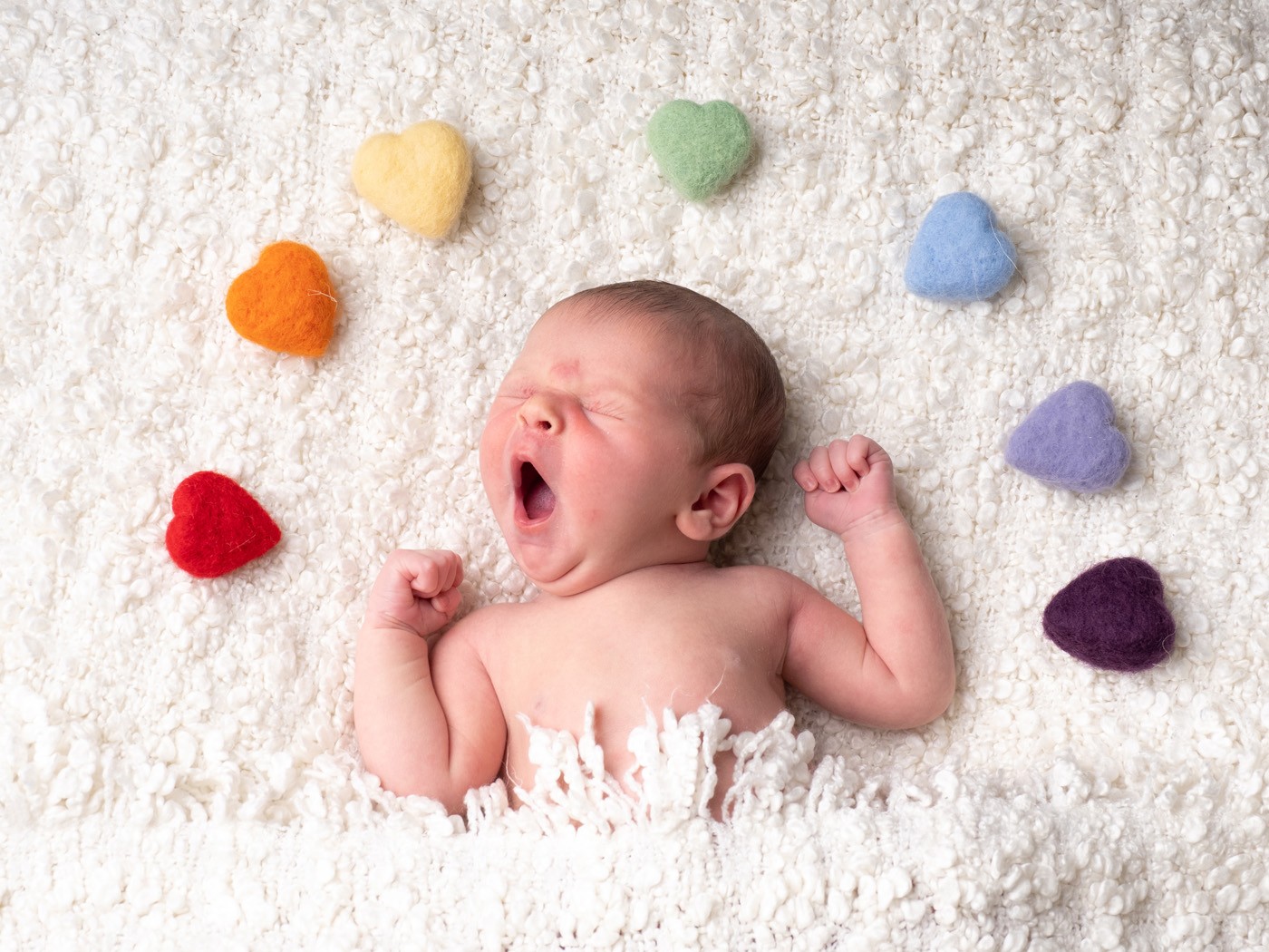 Newborn baby yawning, surrounded by a rainbow of felt hearts
