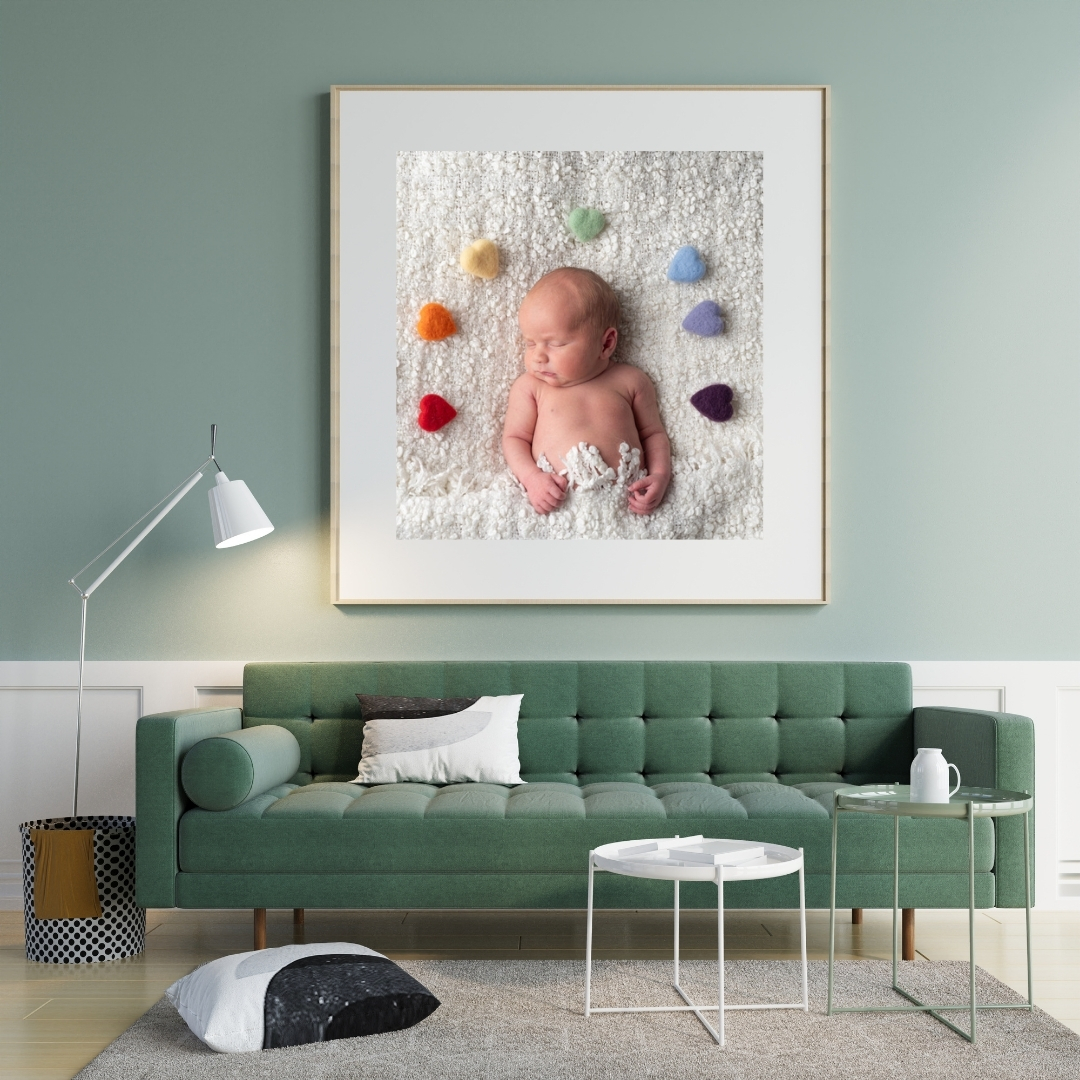Framed rainbow newborn portrait above a green sofa